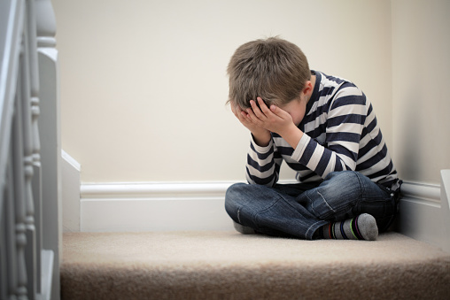 Upset problem child with head in hands sitting on staircase concept for childhood bullying, depression stress or frustration
