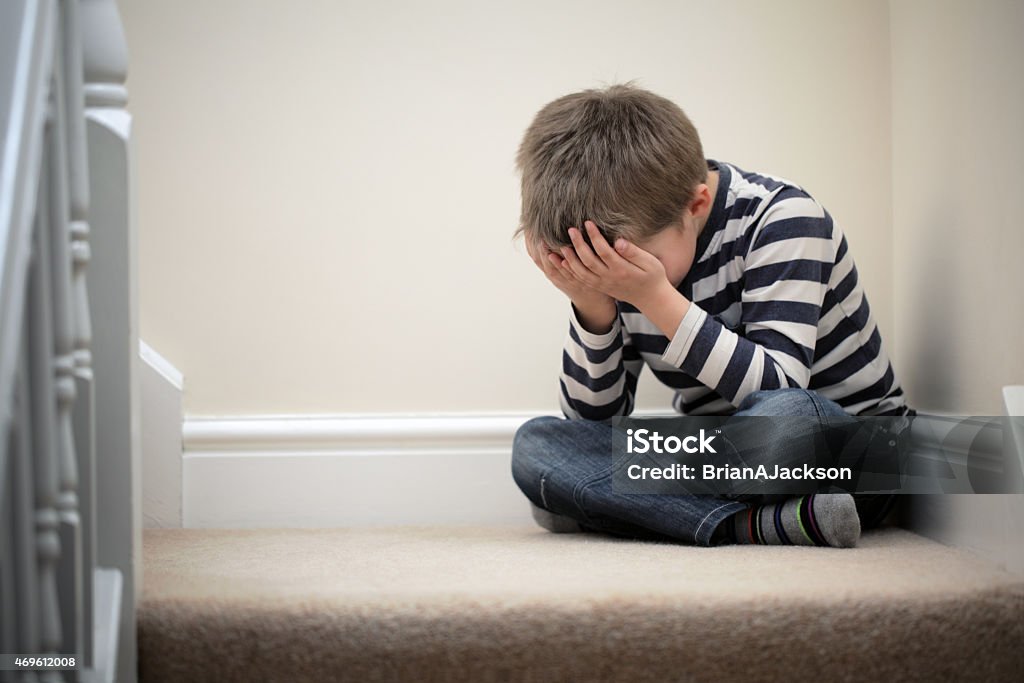 Upset problem child sitting on staircase Upset problem child with head in hands sitting on staircase concept for childhood bullying, depression stress or frustration Child Stock Photo