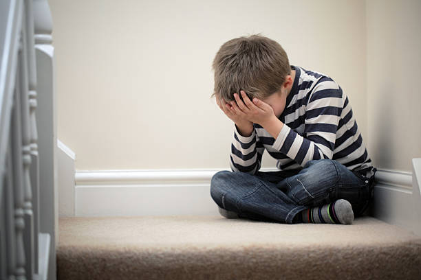 Upset problem child sitting on staircase Upset problem child with head in hands sitting on staircase concept for childhood bullying, depression stress or frustration sulking stock pictures, royalty-free photos & images