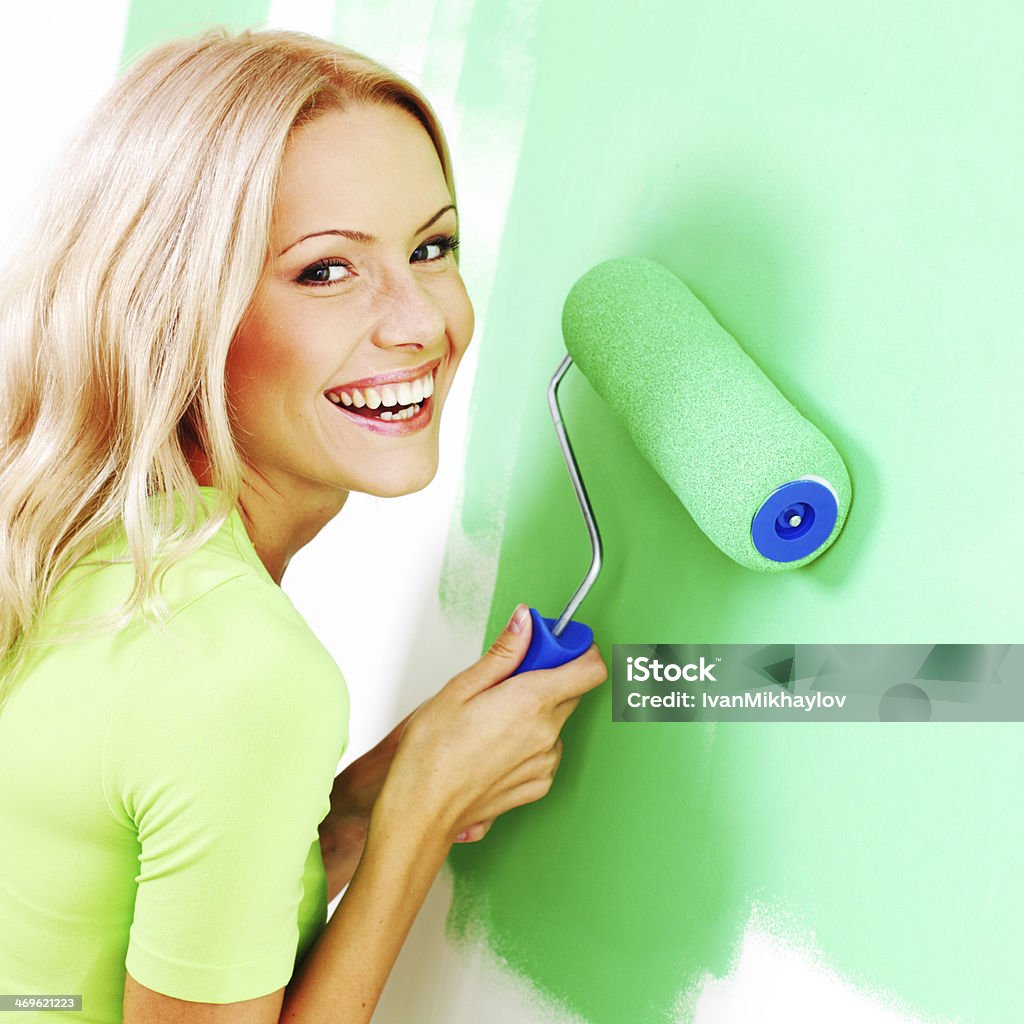 Woman painting the wall Smiling young woman painting the wall with roller brush Paint Stock Photo