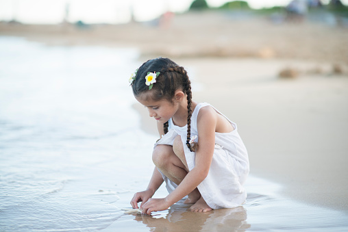 Little girl on vacation playing with a starfish at the beach on the waters edge.