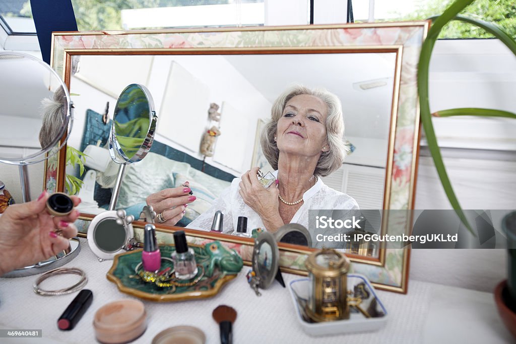 Mirror reflection of senior woman spraying perfume on herself Mirror reflection of senior woman spraying perfume on herself at home 60-69 Years Stock Photo