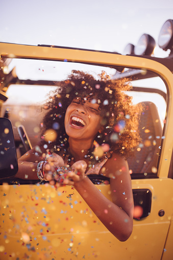 Laughing Afro girl throwing confetti in the back of an open top vacation vehicle on a road trip