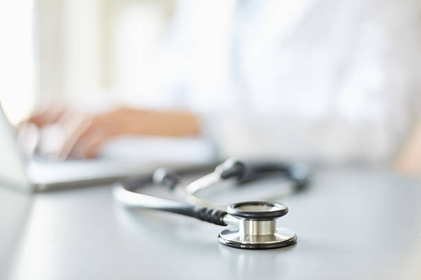 istock Stethoscope on desk with doctor using laptop in background 469645338