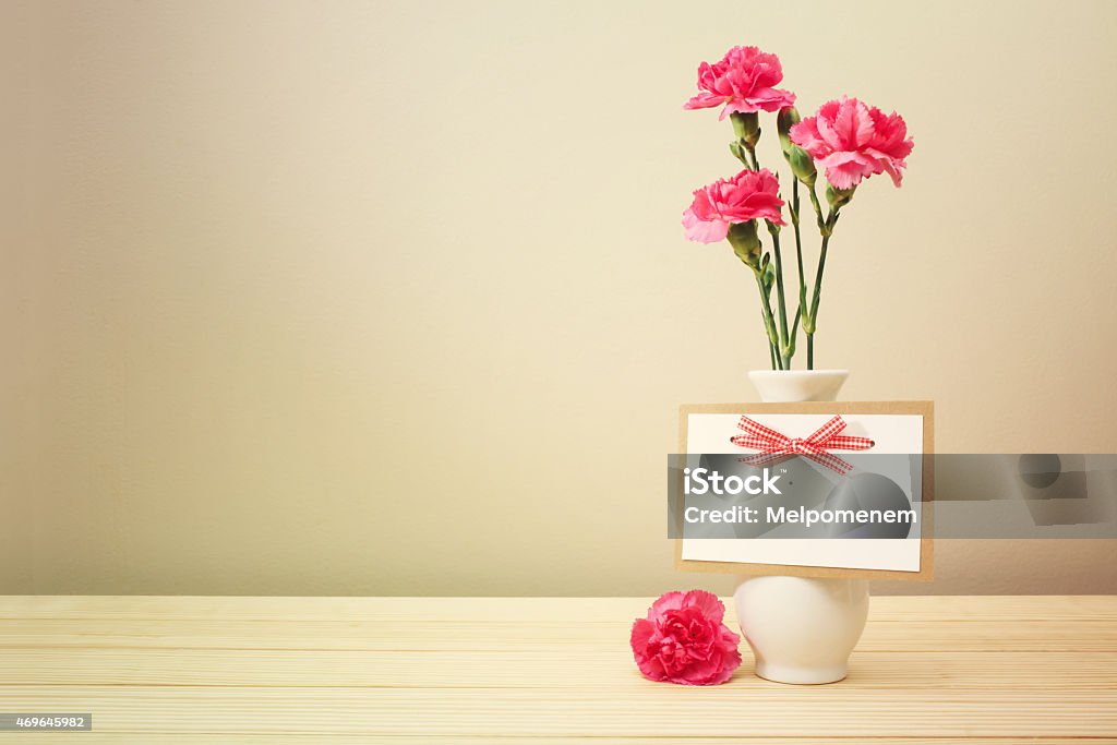 Pink Carnations on White Vase with Blank Greeting Card Pretty Pink Carnation Flowers on White Vase with Blank Greeting Card on Wooden Table with Light Brown Wall Background 2015 Stock Photo