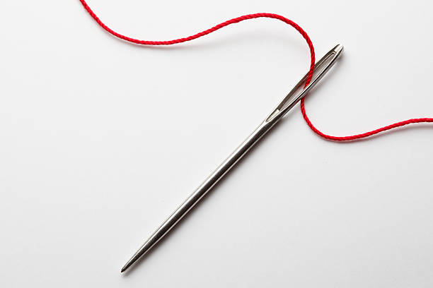 Close up of threading eye of a needle with red thread A close up of the eye of a needle being thread with red thread.  The thread gracefully curves across the image as it makes its way in and out of the eye of the needle.  It is photographed on a white background sewing needle photos stock pictures, royalty-free photos & images