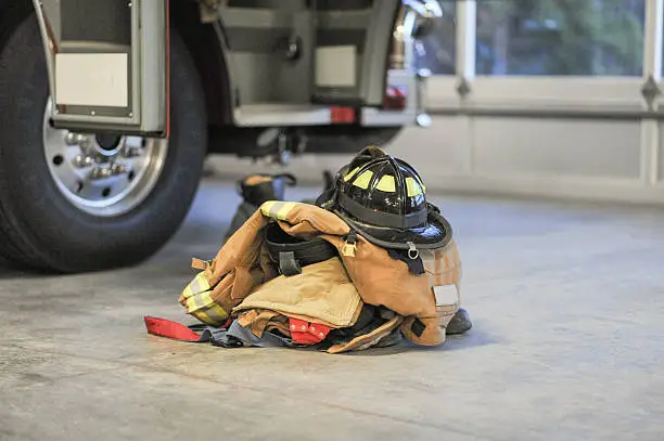 Fire bunker turnout-gear with a helmet is strategically set next to a fire engine in the fire station truck bay ready for a call.