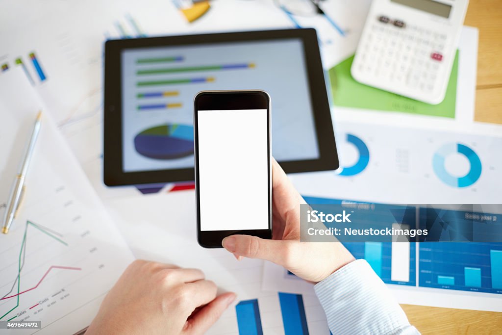 Point of View businesswoman holding smart phone with blank scree Directly above cropped image of businesswoman using smart phone with blank screen. Female executive is at desk with financial documents and digital tablet. The empty space on mobile phone can be used for advertisement purpose. Image is from the point of view of the person. 2015 Stock Photo