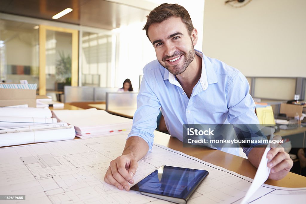 Male Architect With Digital Tablet Studying Plans In Office Male Architect With Digital Tablet Studying Plans In Office Smiling At Camera Architect Stock Photo