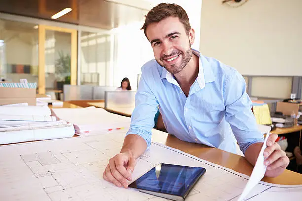 Male Architect With Digital Tablet Studying Plans In Office Smiling At Camera