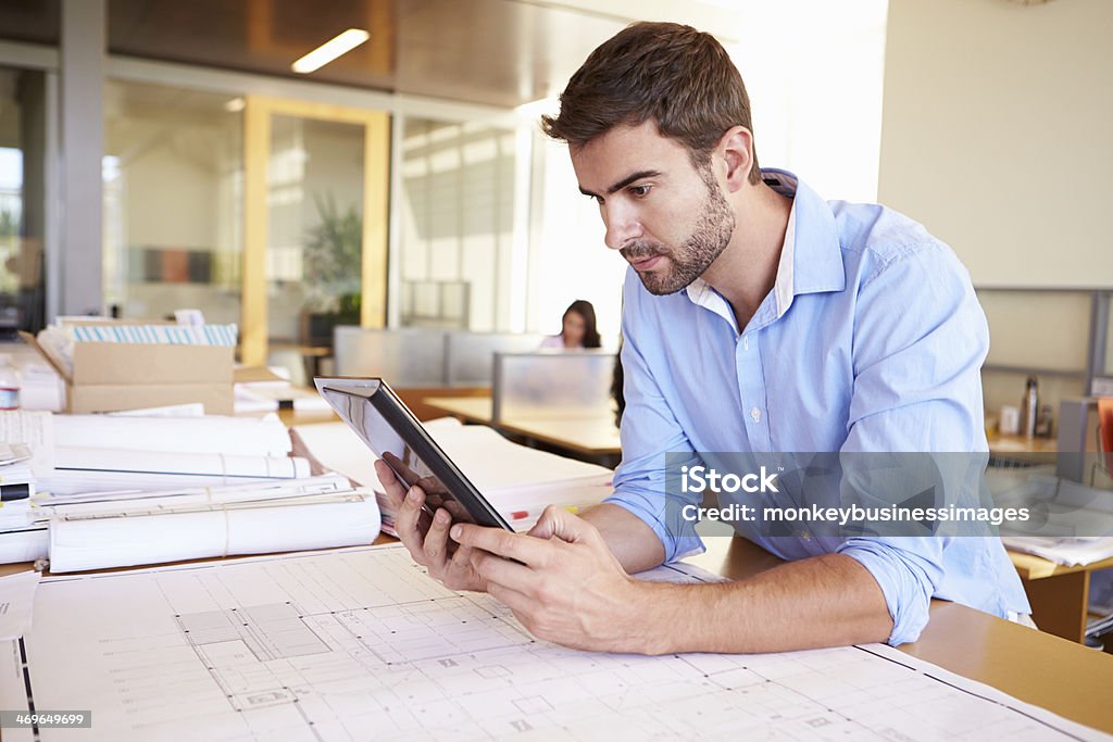 Male Architect With Digital Tablet Studying Plans In Office Male Architect With Digital Tablet Studying Plans In Office In Smart/Casual Dresswear 30-39 Years Stock Photo