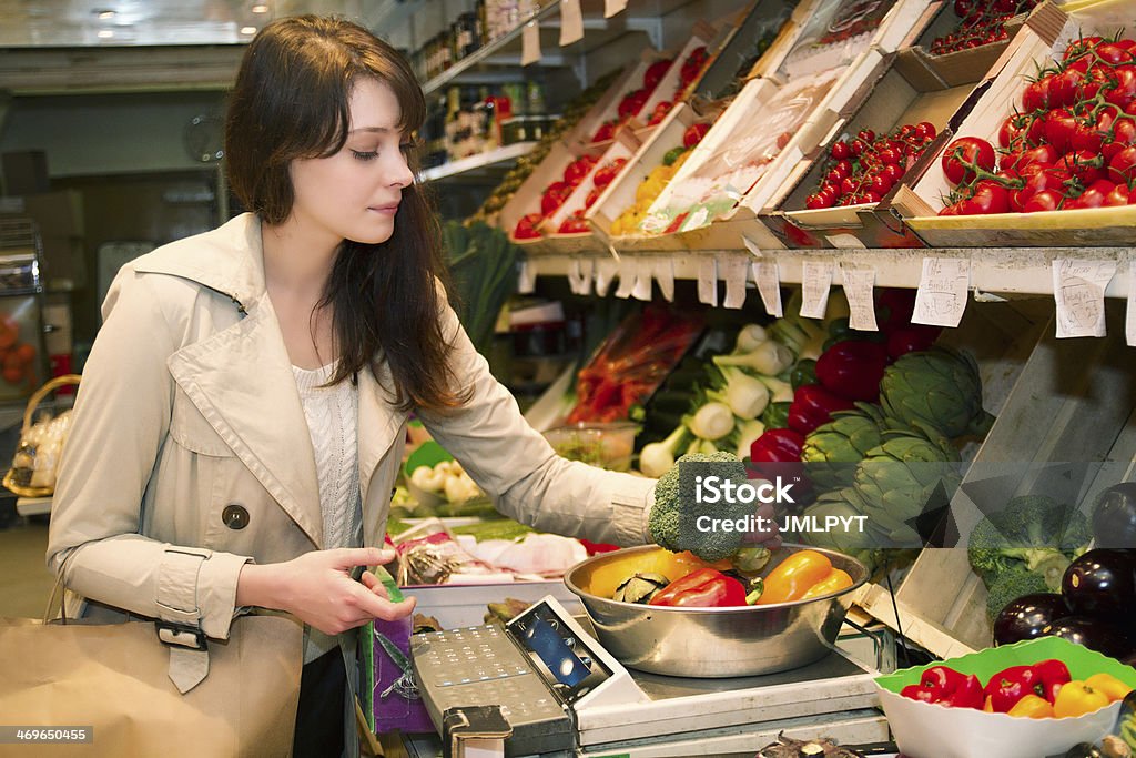 Young woman who weighs vegetables that it is buying Young woman in a fruit and vegetable store choosing what she(it) is going to buy. She(it) has the arm tightened(stretched out) to seize a vegetable (broccolis). Greengrocer's Shop Stock Photo
