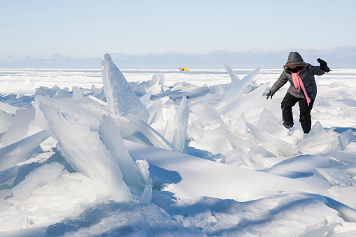 Woman in hooded coat and pink scarf walking over jagged ice on Lake Superior in winter, Apostle Island National Lakeshore, Cornucopia, Bayfield County, Wisconsin, USA