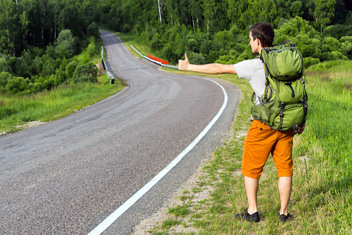 Young man with green backpack hitchhiking on a country road