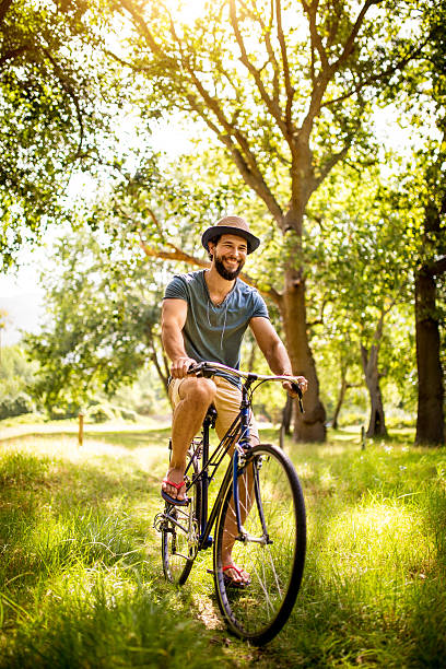 Happy young man laughing and cycling through a sunny park on a summer's day