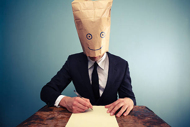 istock Businessman with bag over head writing at desk 469709181