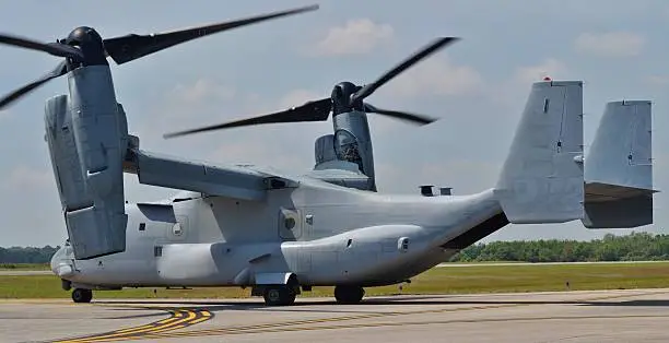A Marine Corps V-22 Osprey tilt-rotor helicopter/airplane preparing for takeoff on a runway. 