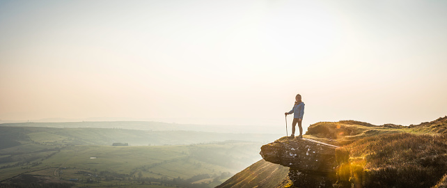 Young girl hiker standing on high mountain ridge looking out over a panoramic vista to the hazy mountain escarpment of the Brecon Beacons National Park, Wales, UK. ProPhoto RGB profile for maximum color fidelity and gamut.