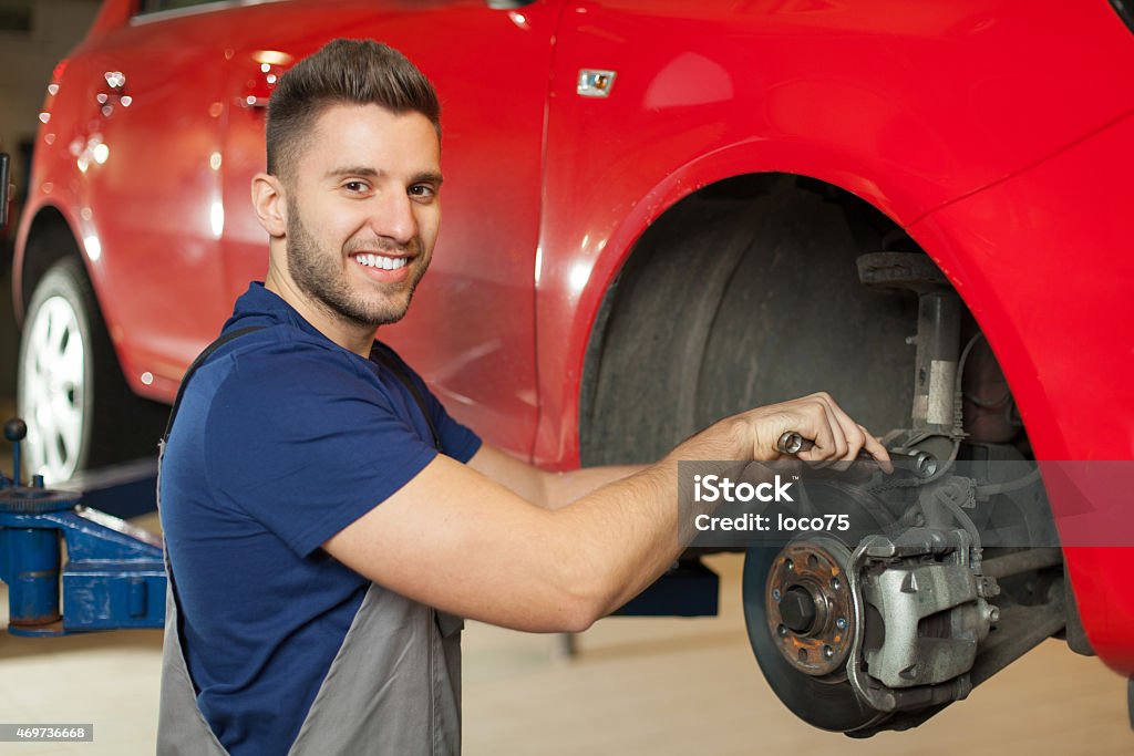 Fixing a car brakes Smiling mechanic repairing a car brakes in auto mechanic shop Motor Vehicle Stock Photo