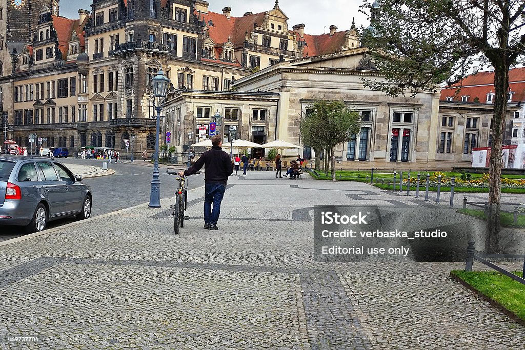 Man walking bike in Dresden Dresden, Germany - September 30, 2014: Unidentified middle-aged man walks his bicycle down in the pavement of Theaterplatz (Theatre Square). This man is photographed from his back. Historical city palaces in the background 2015 Stock Photo