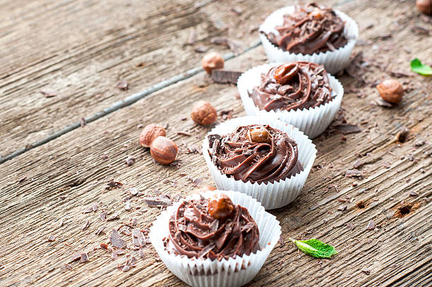 Row of chocolate cupcakes with hazelnuts on top. Wooden background.