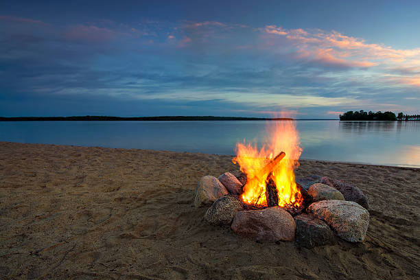 camp fire, accanto al lago al tramonto. minnesota, usa - beach sunset sand wood foto e immagini stock