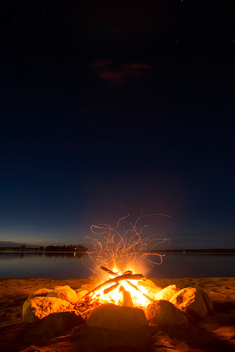 Sparking camp fire beside lake under a starry sky.