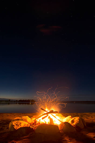 reluzentes descanse perto de fogo de acampamento ao lado do lago sob um céu estrelado. - beach sunset sand wood - fotografias e filmes do acervo