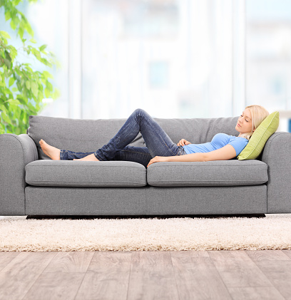 Young blond woman sleeping on a modern gray sofa at home shot with tilt and shift lens