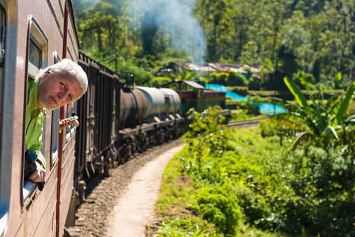 View of a man looking out of a train window in Sri Lanka Mountains between Nuwara Eliya and Ella. It is an old steam train and ride is extremely picturesque with a lot of Tea plantations.