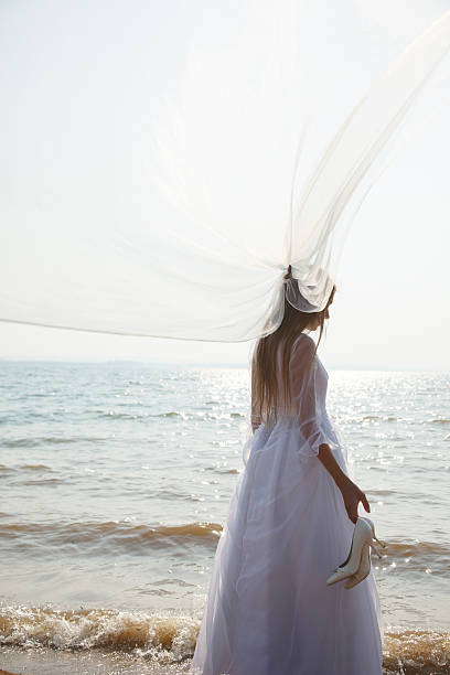 istock Bride is standing on the beach and holding her shoes 469768416
