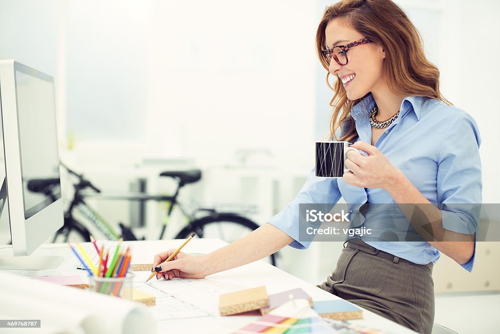 Female Interior Designer Sketching At Work. Smiling female architect working at her office. She is sitting and sketching design. Shallow DOF. Selective focus to beautiful toothy smile. Engineer Stock Photo