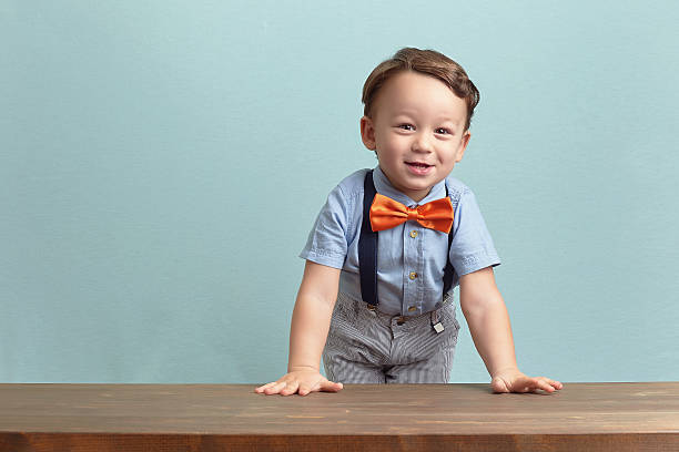 счастливый маленький мальчик в оранжевый галстук и очки - bow looking at camera waist up indoors стоковые фото и изображения