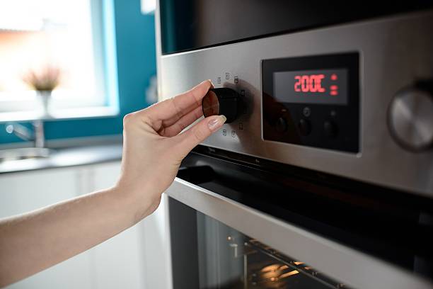 Close up of woman's hand setting temperature control on oven Close up of woman's hand setting temperature control on oven. The display shows the set temperature to 200 degrees Celsius oven door stock pictures, royalty-free photos & images