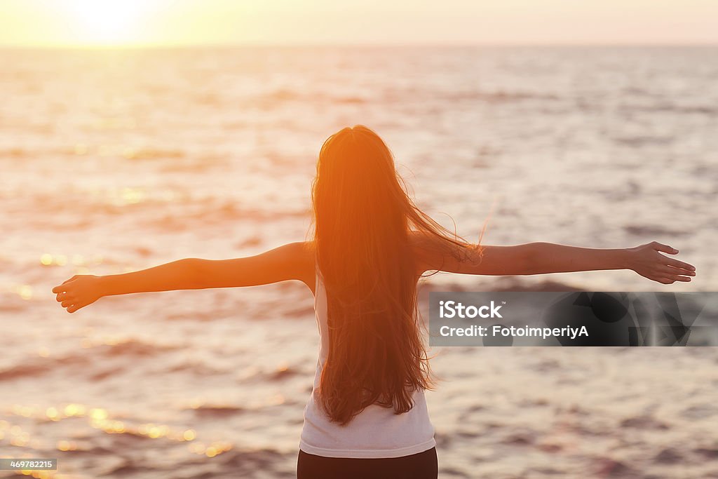 Beach woman laughing having fun Free woman enjoying freedom feeling happy at beach at sunset. Beautiful serene relaxing woman in pure happiness and elated enjoyment with arms raised outstretched up. Asian Caucasian female model. Adult Stock Photo