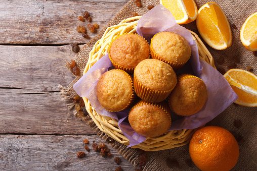 Citrus muffins in a basket and fresh oranges on an old table close-up. horizontal view from above