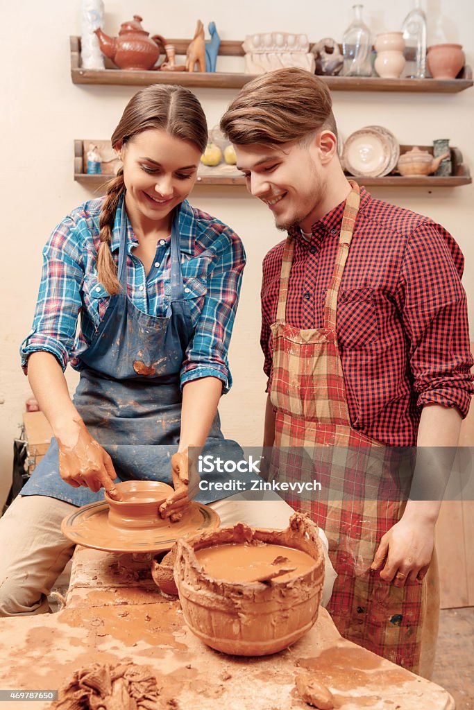 Couple works on the pottery wheel Pleasant work together.  Young female and male potters smiling and shaping on clay pot on the wheel in studio  2015 Stock Photo