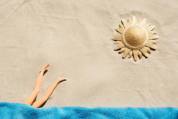 Directly above Antique decorated sun shaped round mirror filled with a heap of gold dust on the beach sand. The fashion doll dives into the sea (towel)