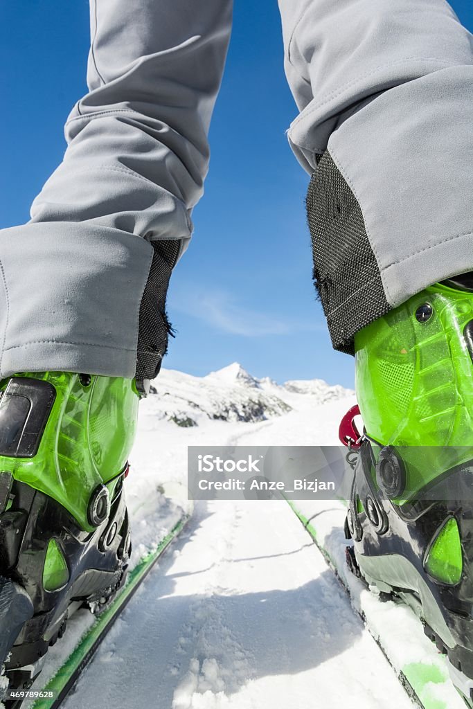 Close up of skier's boots and skis from ground level. Close up of skier's boots and skies from unusual angle. Mountain peak in the background. 2015 Stock Photo