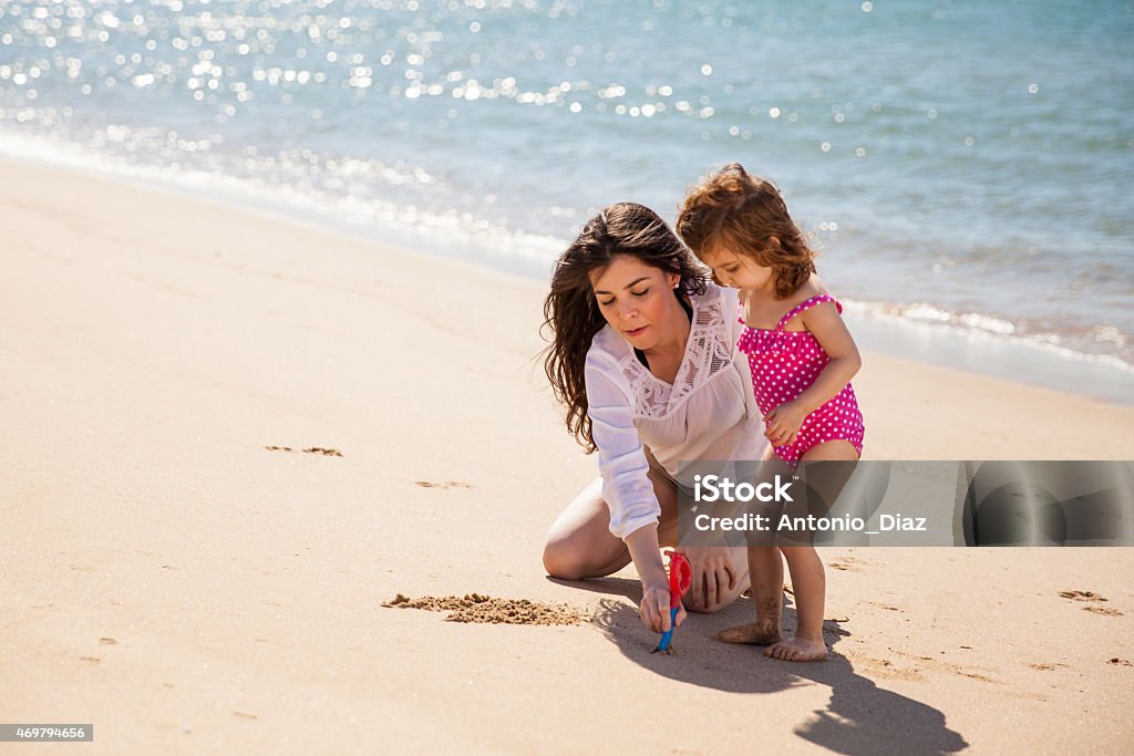 Mom and daughter writing in sand Portrait of a young mother and her little girl drawing something together on the sand 2015 Stock Photo