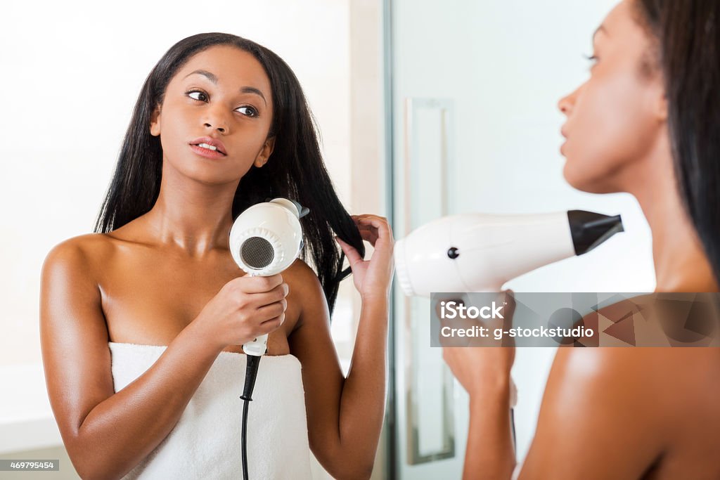 Woman drying hair. Rear view of beautiful young African woman washing hands in bathroom and looking at the mirror Blow Drying Hair Stock Photo