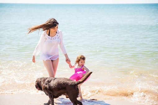 Young brunette with her little daughter and her dog having a good time at the beach