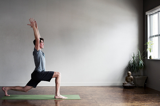 A male yoga instructor does a pose at an indoor yoga studio.