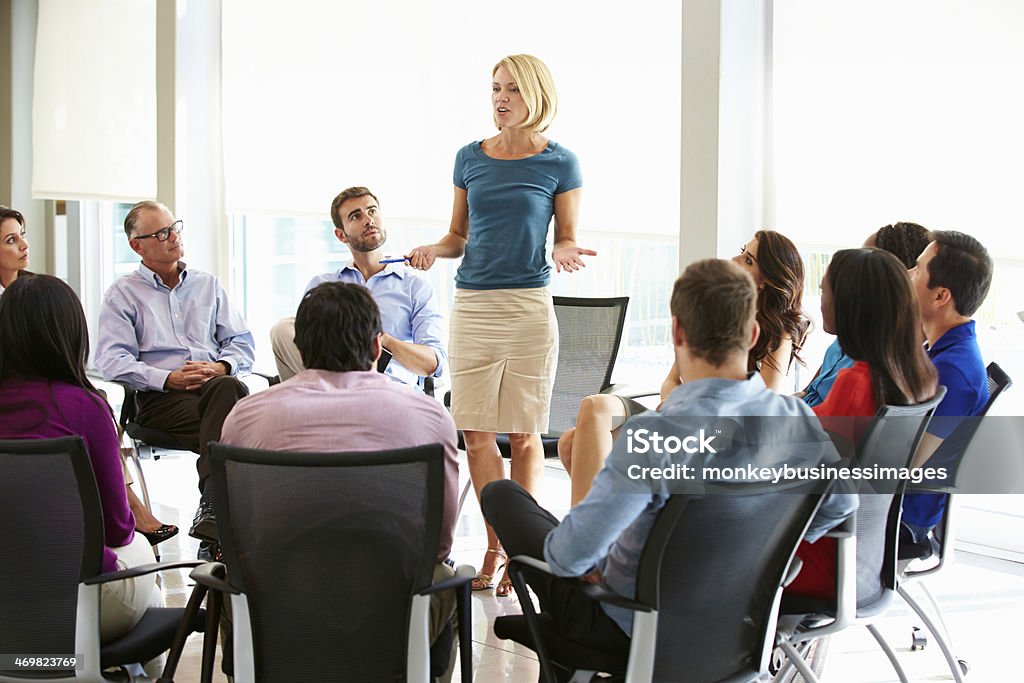 Businesswoman Addressing Multi-Cultural Office Staff Meeting Businesswoman Addressing Multi-Cultural Office Staff Meeting In Smart/Casual Dresswear Chair Stock Photo