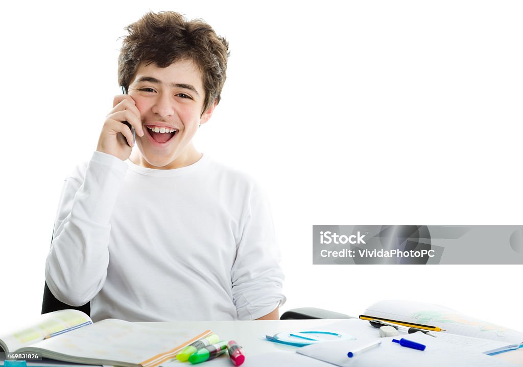 Caucasian smooth-skinned boy talking on cell phone on homeworks Smiling handsome Caucasian smooth-skinned boy is talking on cell phone while doing homework and wearing a white long sleeve t-shirt 2015 Stock Photo
