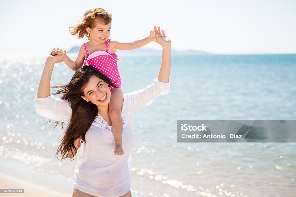 Piggybacking my mom at the beach Portrait of a pretty little girl piggyback riding her mother while spending the day in the beach 2015 Stock Photo