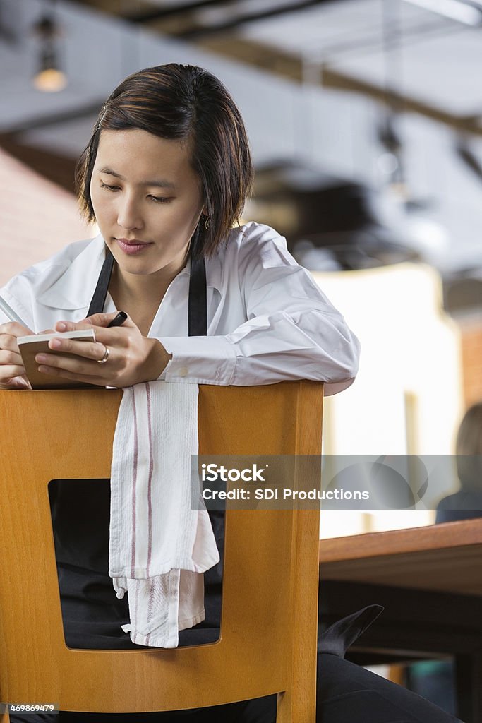 Asian waitress reviewing tickets in restaurant after closing Apron Stock Photo