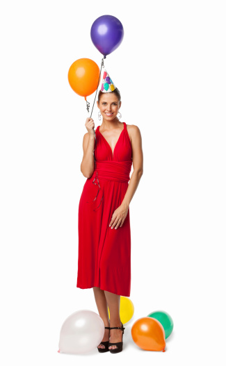 Full length portrait of an attractive young woman in red dress with balloons and party hat. Vertical shot. Isolated on white.