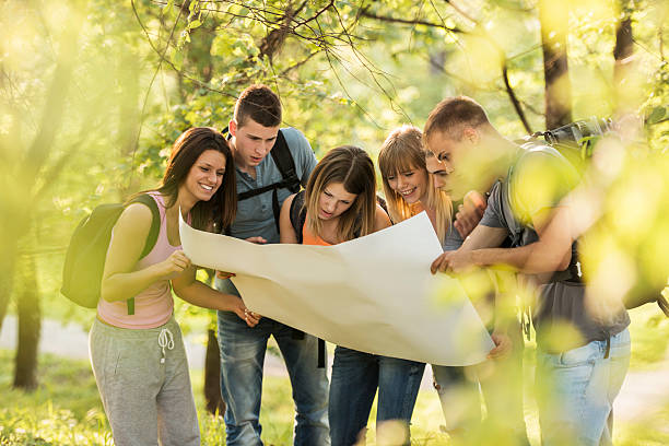 Teenagers looking at map. Group of teenagers standing in the forest and looking at map.   orienteering stock pictures, royalty-free photos & images