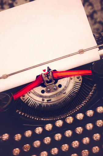 Vintage toned image of a vintage typewriter with red ribbon and a heart printed on the paper to suggest the concept Love to Write or writing a Love Story.